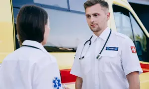 Dwóch ratowników medycznych w białych koszulach rozmawia obok karetki. Chcesz wiedzieć, jak zostać ratownikiem medycznym?