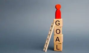 Drewniane klocki z literami GOAL, drabinka i czerwona figurka symbolizująca cel.