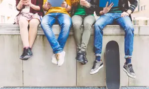 Grupa młodych ludzi, prawdopodobnie pokolenie Z, spędza czas na świeżym powietrzu, każdy zajęty swoim urządzeniem lub książką.
