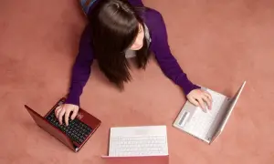 Kobieta leży na dywanie i pisze na trzech laptopach.