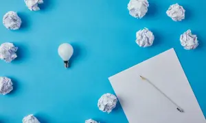 Zgniecione kartki papieru i żarówka symbolizują proces tworzenia, gdy zastanawiasz się, jak napisać list motywacyjny.