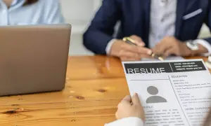 Osoba przegląda CV, szukając kluczowych umiejętności do cv. Obok leży laptop.