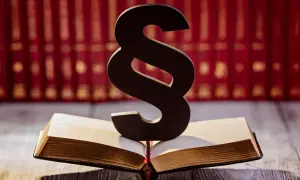Symbol paragrafu na otwartej księdze, sugerujący upomnienie dla pracownika. W tle rząd czerwonych ksiąg.