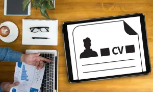 Tablet z ikoną CV i sylwetką mężczyzny, obok laptop, notatnik, okulary i kawa.