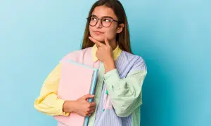 Młoda kobieta w okularach z zeszytami zastanawia się nad ciekawymi kierunkami studiów dla niezdecydowanych.