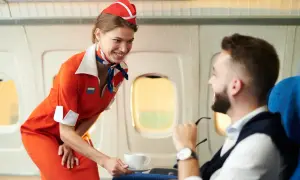 Uśmiechnięta stewardessa w pomarańczowym stroju podaje kawę pasażerowi w samolocie.