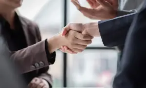 Dwie osoby ściskają sobie dłonie, symbolizując porozumienie i nowy układ zbiorowy pracy.