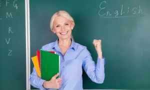 Uśmiechnięta nauczycielka z zeszytami, zaciśnięta pięść symbolizuje sukces w nauczaniu. Jej pensum nauczyciela jest pełne wyzwań, ale i satysfakcji.