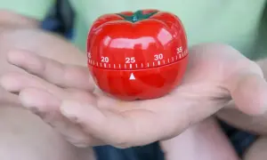 Czerwony minutnik w kształcie pomidora, idealny do metody pomodoro, spoczywa na dłoni.