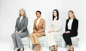 Cztery kobiety w garniturach siedzą na krzesłach, prezentując różne interpretacje dress code'u.