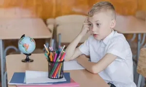 Chłopiec zamyślony przy biurku, na którym leży globus i przybory. Obowiązek szkolny bywa trudny.