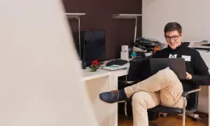 Uśmiechnięty mężczyzna w okularach pracuje na laptopie. Zastanawia się, czy działalność gospodarcza wlicza się do stażu pracy.