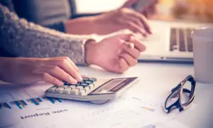 Ręce pracujące przy kalkulatorze i laptopie, analizujące raporty. Może to być początek planowania budżetu na dieta zagraniczna.