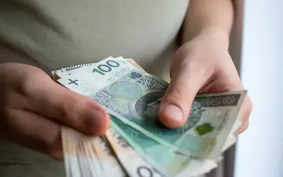 Dłonie trzymają stos banknotów 100 zł. To kwota, która dla wielu jest znacząca, ale w kontekście dużych inwestycji może być traktowana jako de minimis.