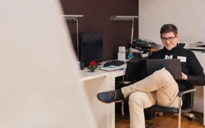 Uśmiechnięty mężczyzna w okularach pracuje na laptopie. Zastanawia się, czy działalność gospodarcza wlicza się do stażu pracy.