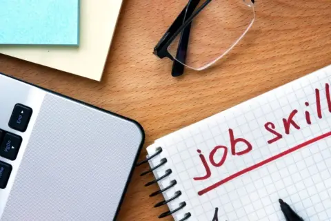 Notatnik z napisem "job skills", laptop i okulary. Przygotowanie do autoprezentacji.