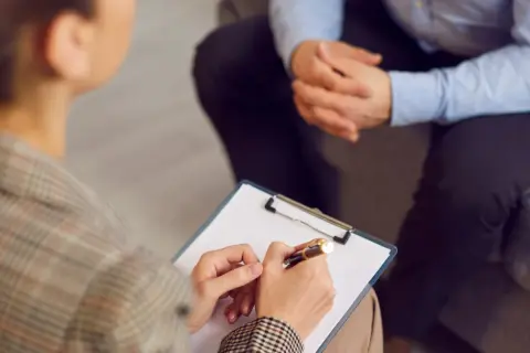 Sesja terapeutyczna, gdzie psychoterapeuta notuje ważne informacje. To obraz postępu w kierunku regulacji zawodu, jak ustawa o zawodzie psychoterapeuty.