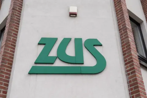 Zielone logo ZUS na jasnej ścianie budynku z ceglanymi elementami.