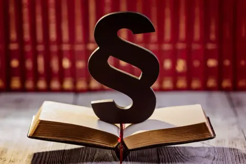 Symbol paragrafu na otwartej księdze, sugerujący upomnienie dla pracownika. W tle rząd czerwonych ksiąg.
