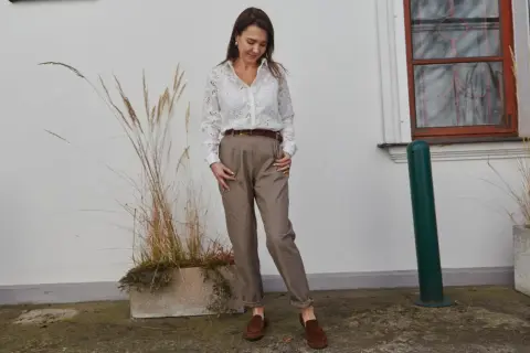 Elegancka stylizacja, która podpowie, jak się ubrać na rozmowę o pracę: biała koszula z ażurowymi detalami, brązowe spodnie i mokasyny.