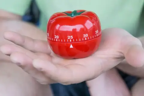 Czerwony minutnik w kształcie pomidora, idealny do metody pomodoro, spoczywa na dłoni.
