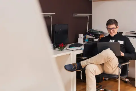 Uśmiechnięty mężczyzna w okularach pracuje na laptopie. Zastanawia się, czy działalność gospodarcza wlicza się do stażu pracy.