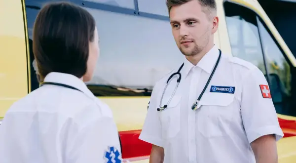 Dwóch ratowników medycznych w białych koszulach rozmawia obok karetki. Chcesz wiedzieć, jak zostać ratownikiem medycznym?