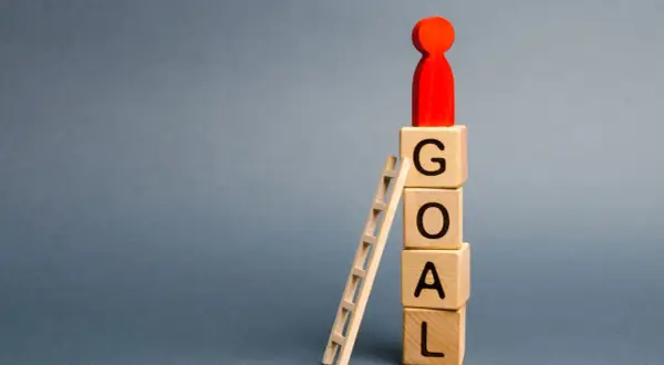 Drewniane klocki z literami GOAL, drabinka i czerwona figurka symbolizująca cel.