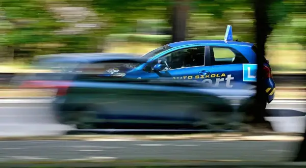 Niebieski samochód z napisem "AUTO SZKOŁA" i literą "L" na drzwiach, w ruchu. Idealny do kursu na instruktora nauki jazdy.