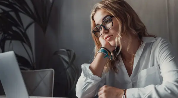 Kobieta w okularach opiera głowę na dłoni, patrząc na laptopa. Brak jej motywacji do pracy, ale wierzy, że cel jest blisko.