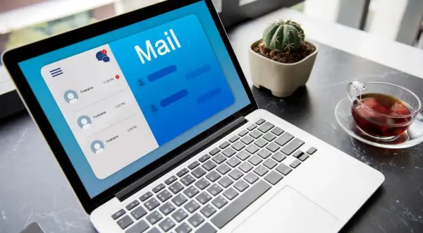 Laptop z otwartą aplikacją poczty, pokazującą jak napisać maila z CV. Obok filiżanka herbaty i mały kaktus.