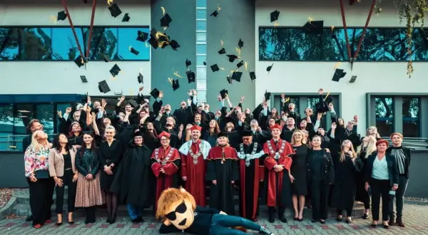Absolwenci w togach rzucają czapki do góry, świętując zakończenie studiów dualnych. Radosna atmosfera i symboliczne pożegnanie z uczelnią.