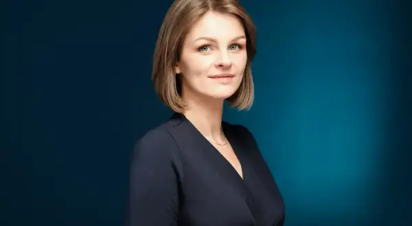 Profesjonalne zdjęcie do CV: uśmiechnięta kobieta z krótkimi blond włosami, w granatowej bluzce, na ciemnoniebieskim tle.