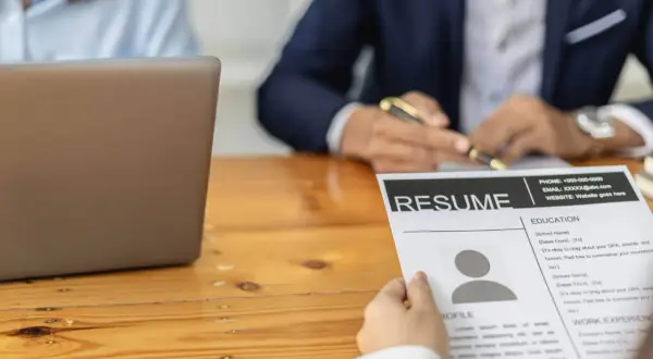 Osoba przegląda CV, szukając kluczowych umiejętności do cv. Obok leży laptop.