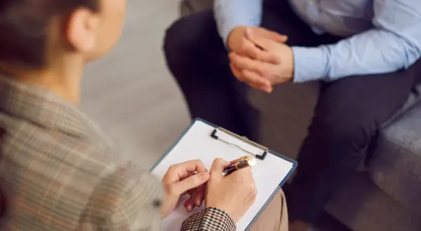 Sesja terapeutyczna, gdzie psychoterapeuta notuje ważne informacje. To obraz postępu w kierunku regulacji zawodu, jak ustawa o zawodzie psychoterapeuty.