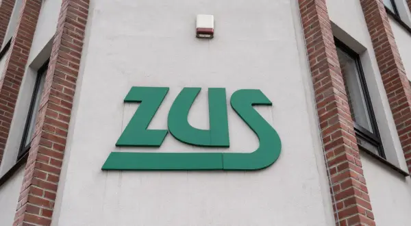 Zielone logo ZUS na jasnej ścianie budynku z ceglanymi elementami.