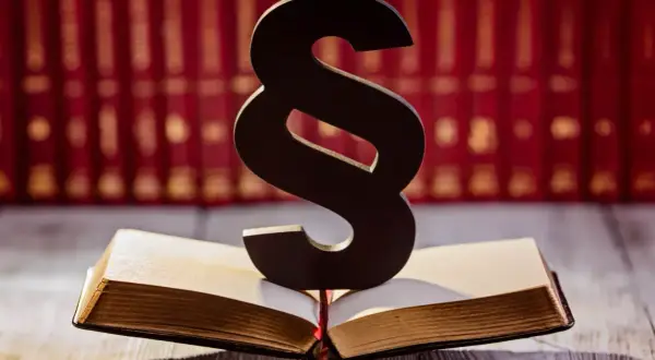 Symbol paragrafu na otwartej księdze, sugerujący upomnienie dla pracownika. W tle rząd czerwonych ksiąg.