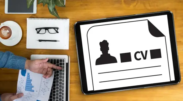 Tablet z ikoną CV i sylwetką mężczyzny, obok laptop, notatnik, okulary i kawa.