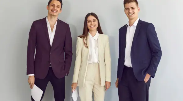 Trzy uśmiechnięte osoby w eleganckich strojach. Idealny przykład, co ubrać na rozmowę kwalifikacyjną.