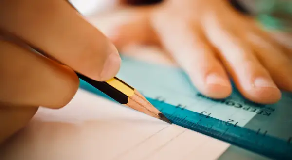 Dłoń z ołówkiem i linijką tworzy zindywidualizowana ścieżka kształcenia, rysując precyzyjne linie na papierze.