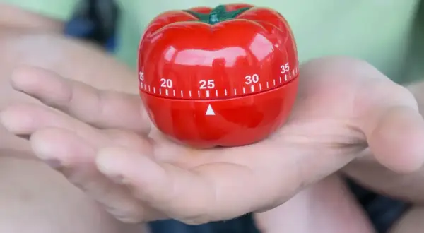 Czerwony minutnik w kształcie pomidora, idealny do metody pomodoro, spoczywa na dłoni.