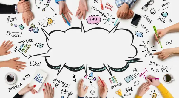 Ludzie tworzą burzę mózgów, rysując na stole słowa: teamwork, idea, plan, vision, share, think, talk, growth, success.