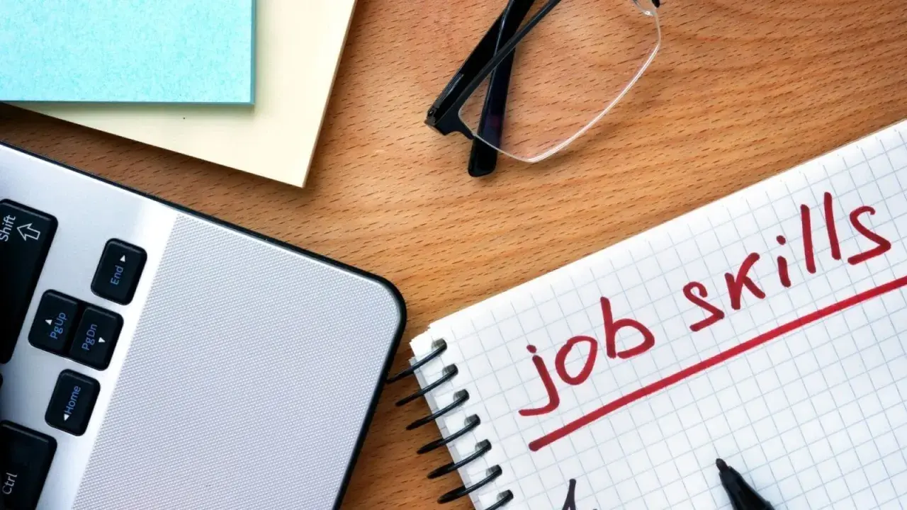 Notatnik z napisem "job skills", laptop i okulary. Przygotowanie do autoprezentacji.
