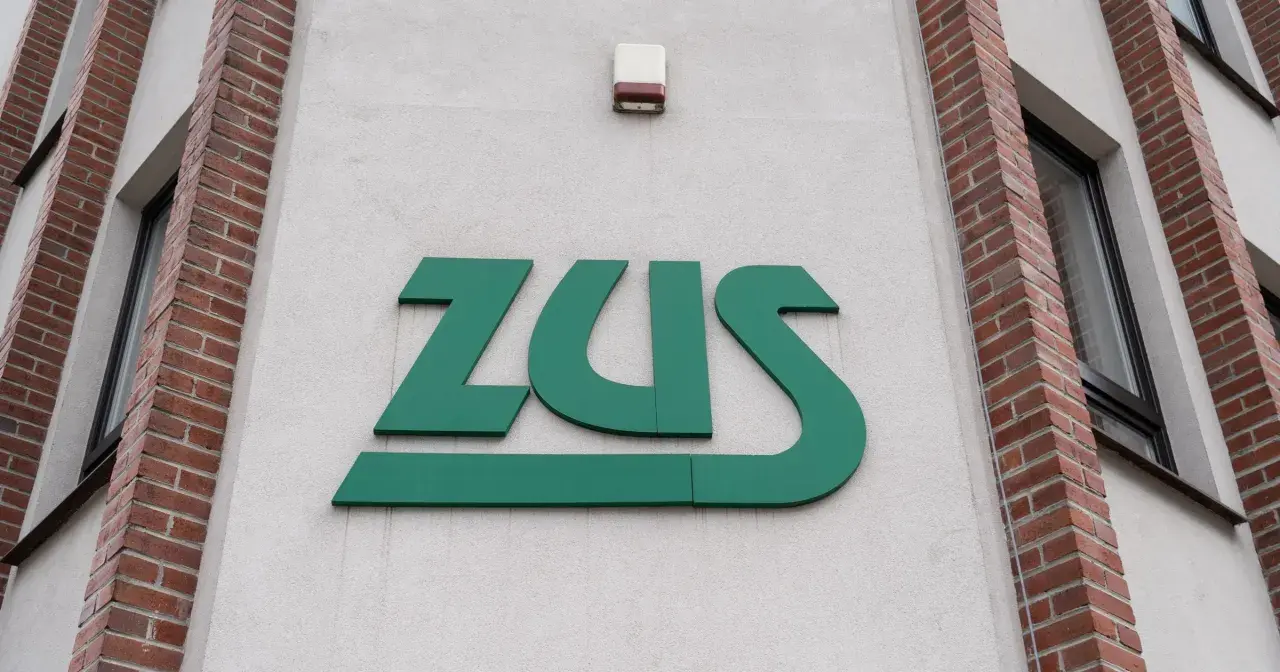 Zielone logo ZUS na jasnej ścianie budynku z ceglanymi elementami.