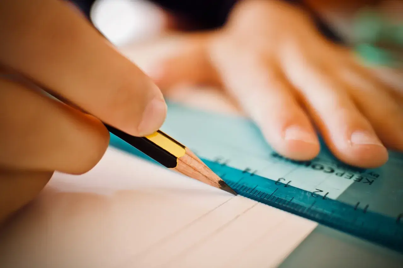 Dłoń z ołówkiem i linijką tworzy zindywidualizowana ścieżka kształcenia, rysując precyzyjne linie na papierze.