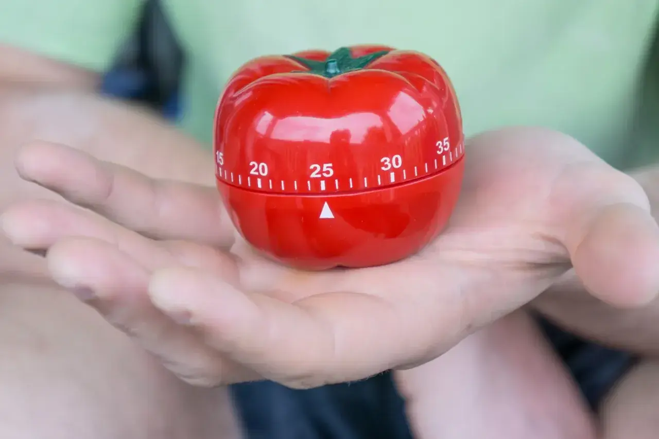 Czerwony minutnik w kształcie pomidora, idealny do metody pomodoro, spoczywa na dłoni.
