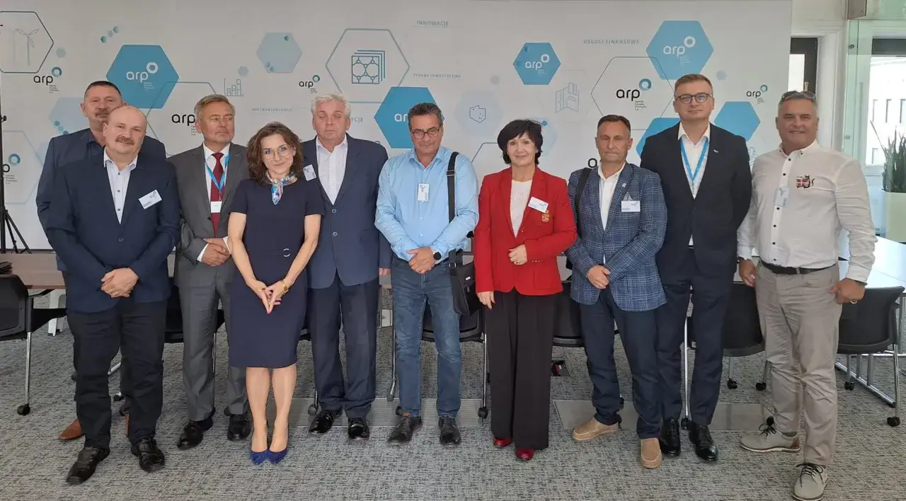 Grupa osób w eleganckich strojach pozuje do zdjęcia na tle ściany z logo ARP. Wszyscy mają przypięte identyfikatory, co sugeruje ważne spotkanie, być może dotyczące współpracy związków zawodowych.