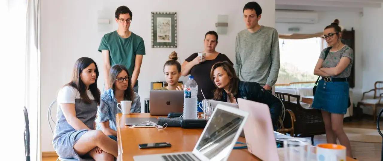 Grupa młodych ludzi, w tym pracownik młodociany, pochyla się nad laptopami, dyskutując o projekcie.