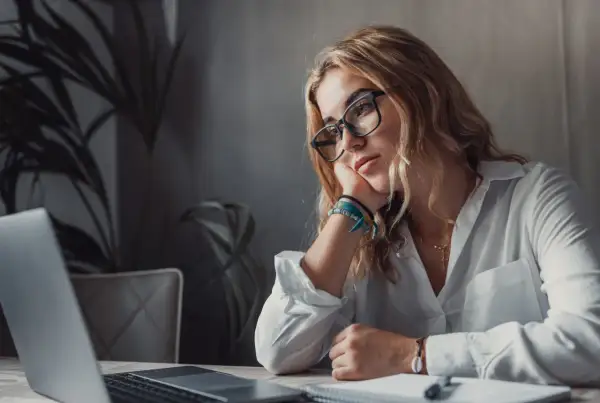 Kobieta w okularach opiera głowę na dłoni, patrząc na laptopa. Brak jej motywacji do pracy, ale wierzy, że cel jest blisko.