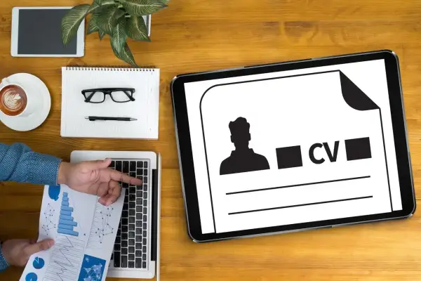 Tablet z ikoną CV i sylwetką mężczyzny, obok laptop, notatnik, okulary i kawa.